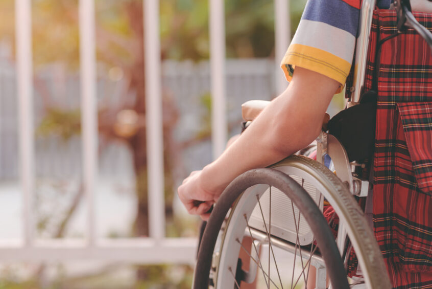 Close view of a person seated in a wheelchair beside a sunlit outdoor railing.