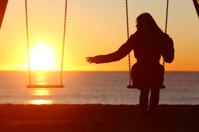 A person sitting alone on a swing, silhouetted against a sunset over the water